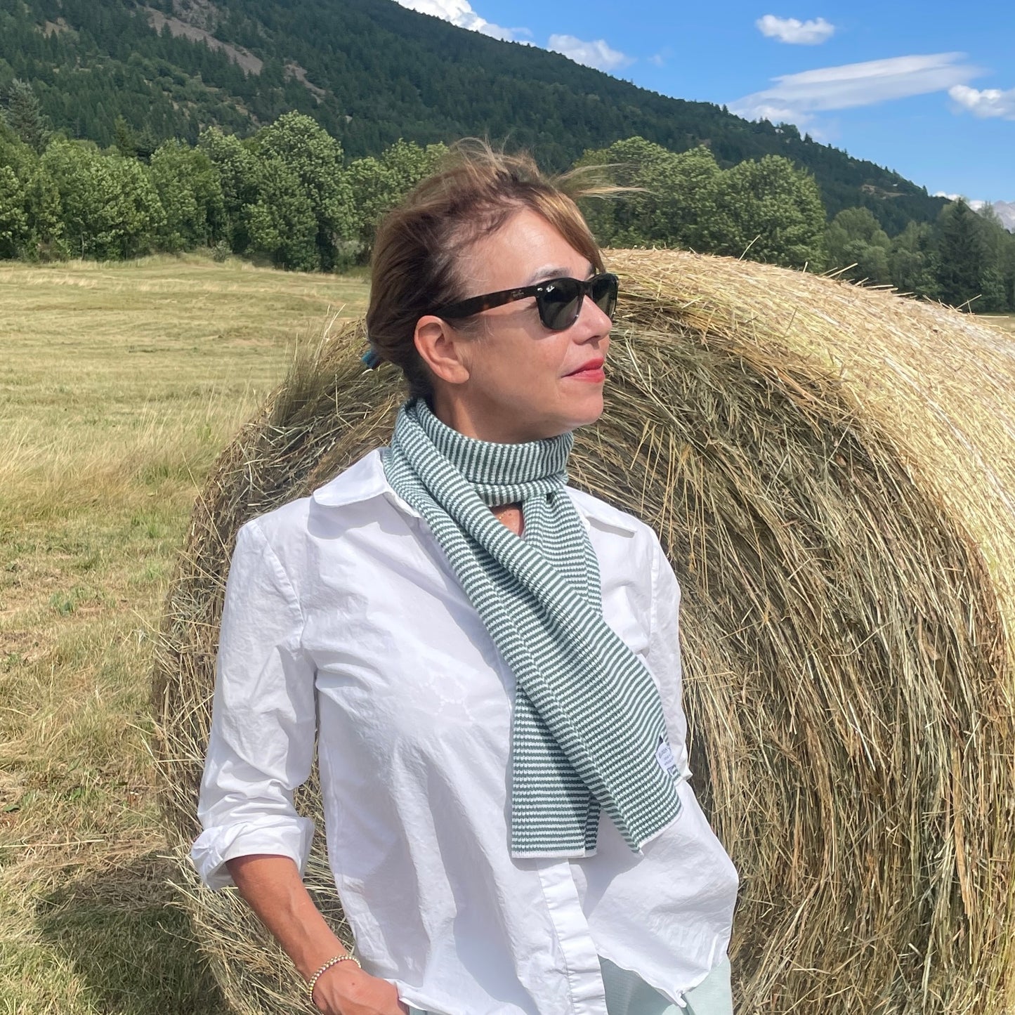 Woman standing next to a hay bale in a field with mountains in the background